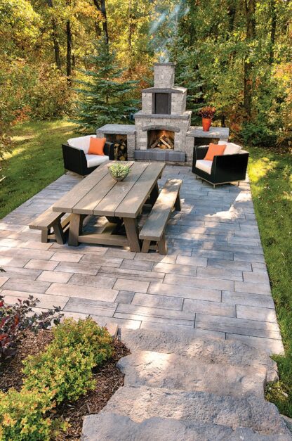Quarry stone outdoor fireplace from Barkman Concrete, available at Ron Paul Garden Centre, displayed on a stone patio with decorative landscaping and a picnic table.