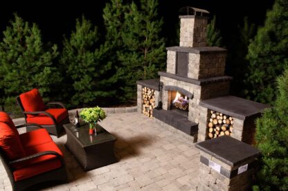 Quarry stone outdoor fireplace from Barkman Concrete, available at Ron Paul Garden Centre, displayed on a stone patio with cozy seating and landscaped garden accents.