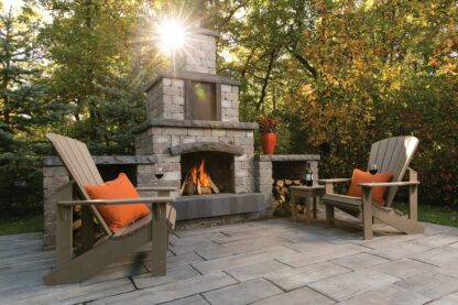 Quarry stone outdoor fireplace by Barkman Concrete, available at Ron Paul Garden Centre. Showcased on a stone patio with seating and a lit fire in the fireplace.